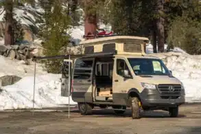 Campervan auf Mercedes-Benz-Sprinter-Basis mit Aufstelldach, Markise und Skiern im Schnee