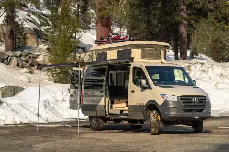 Campervan auf Mercedes-Benz-Sprinter-Basis mit Aufstelldach, Markise und Skiern im Schnee