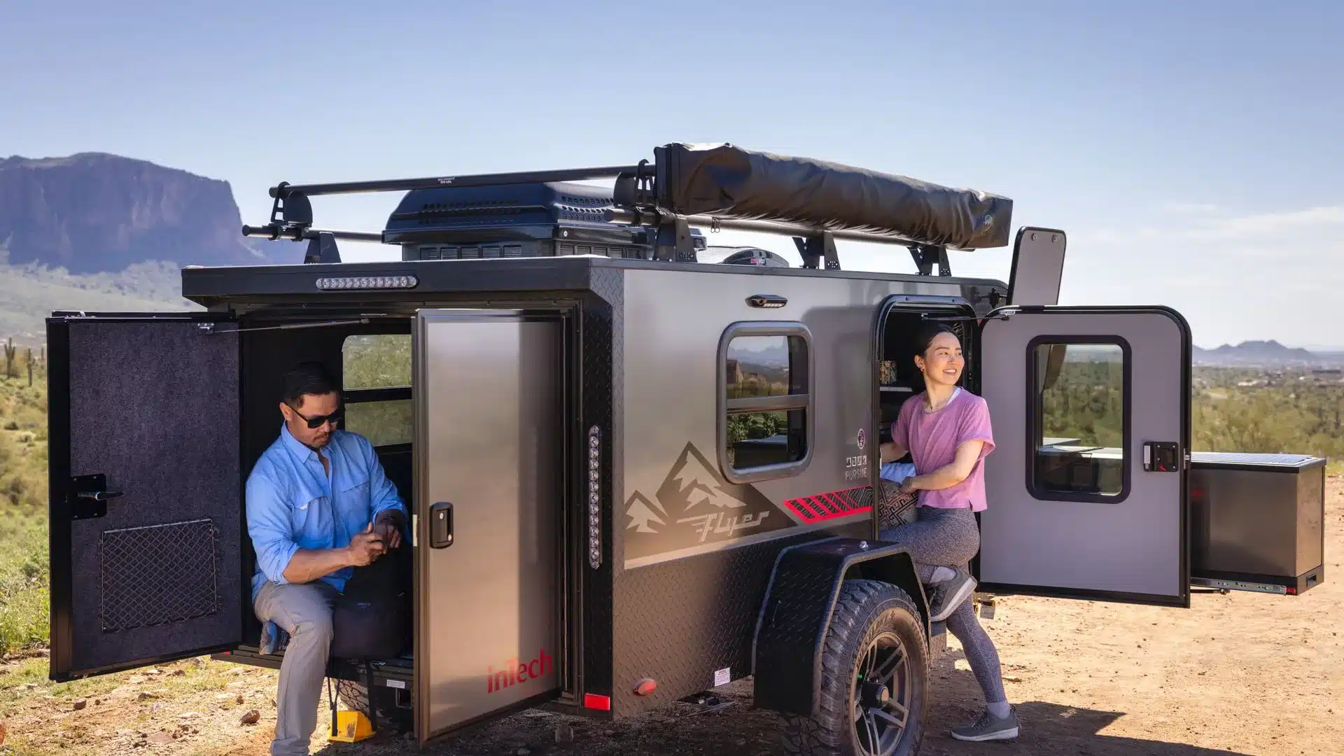 Flyer Pursue Offroad-Campinganhänger mit geöffneter Außenküche und zwei Personen in einer Wüstenlandschaft