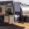 Flyer Pursue Offroad-Campinganhänger mit geöffneter Außenküche, Kühlschrank und Stauraum in einer trockenen Landschaft