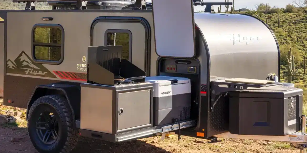 Flyer Pursue Offroad-Campinganhänger mit geöffneter Außenküche, Kühlschrank und Stauraum in einer trockenen Landschaft