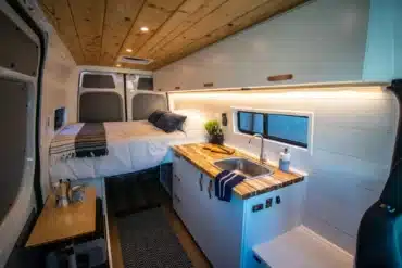 Innenraum eines Campervans mit Bett, Holzdecke, Küchenzeile und Edelstahlspüle