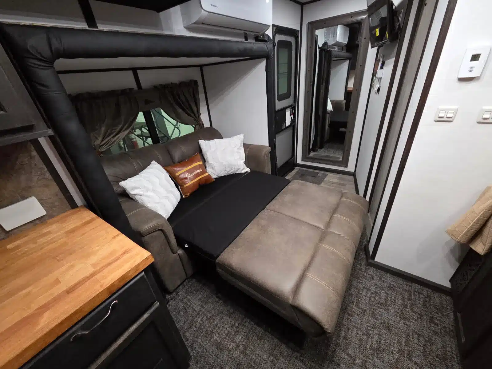 Innenansicht des Wohnbereichs im Ram 5500 Laramie Custom Car Hauler mit Schlafsofa, Tisch und Küchenzeile
