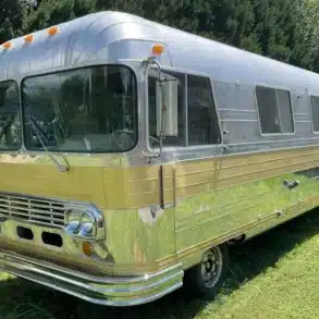 Front-Seitenansicht eines 1966 Streamline Travel Home mit silberner Aluminiumkarosserie und goldfarbenen Zierleisten auf einer Wiese