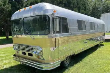Front-Seitenansicht eines 1966 Streamline Travel Home mit silberner Aluminiumkarosserie und goldfarbenen Zierleisten auf einer Wiese