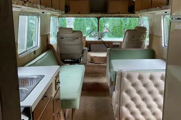 Innenraum eines 1966 Streamline Travel Home mit Küchenzeile, grüner Sitzbank, Dinette und Fahrerhaus