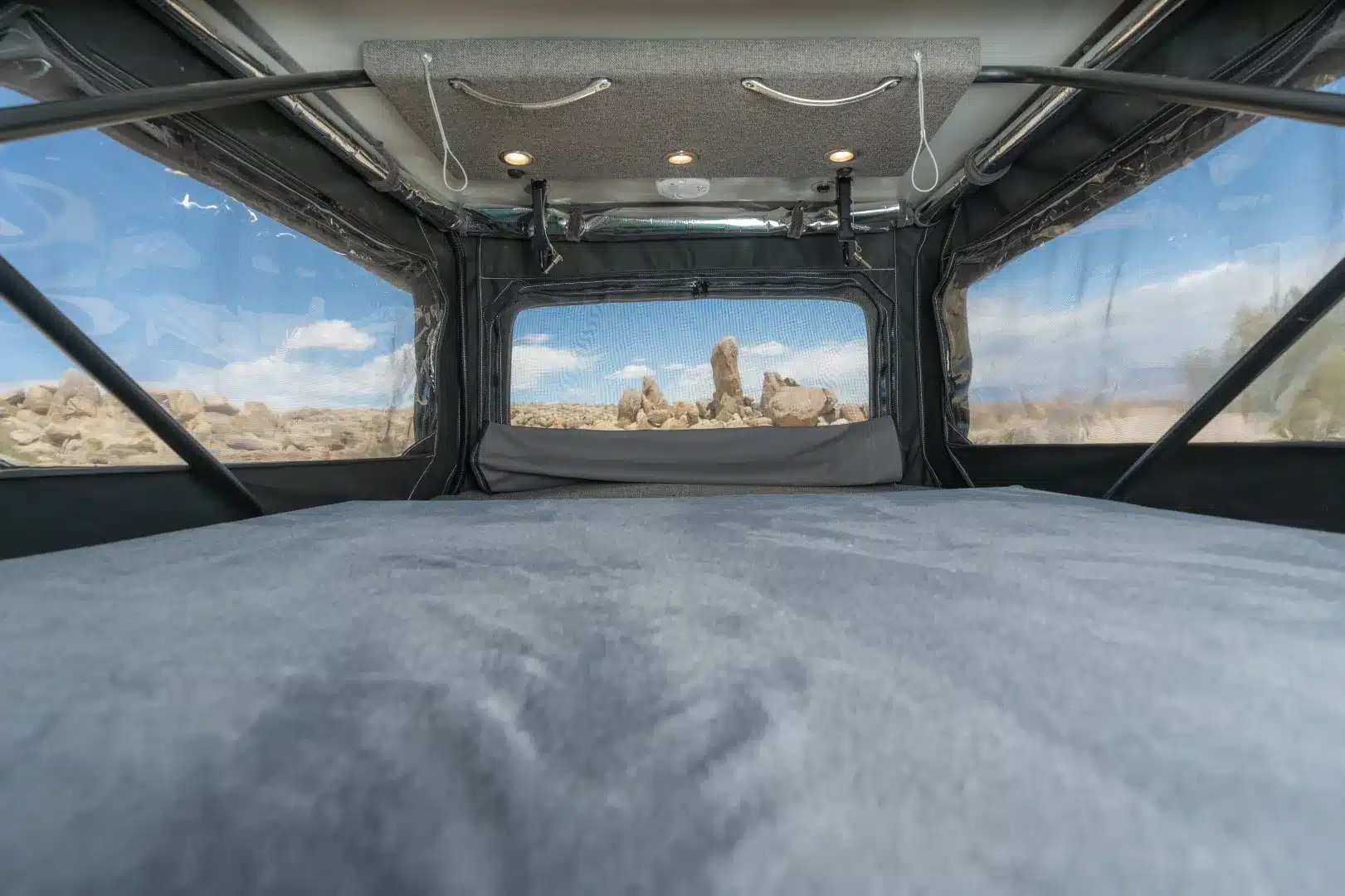 Bett im geöffneten Pop-Top eines Tamarack-Campervans mit Fenster und grauer Innenverkleidung