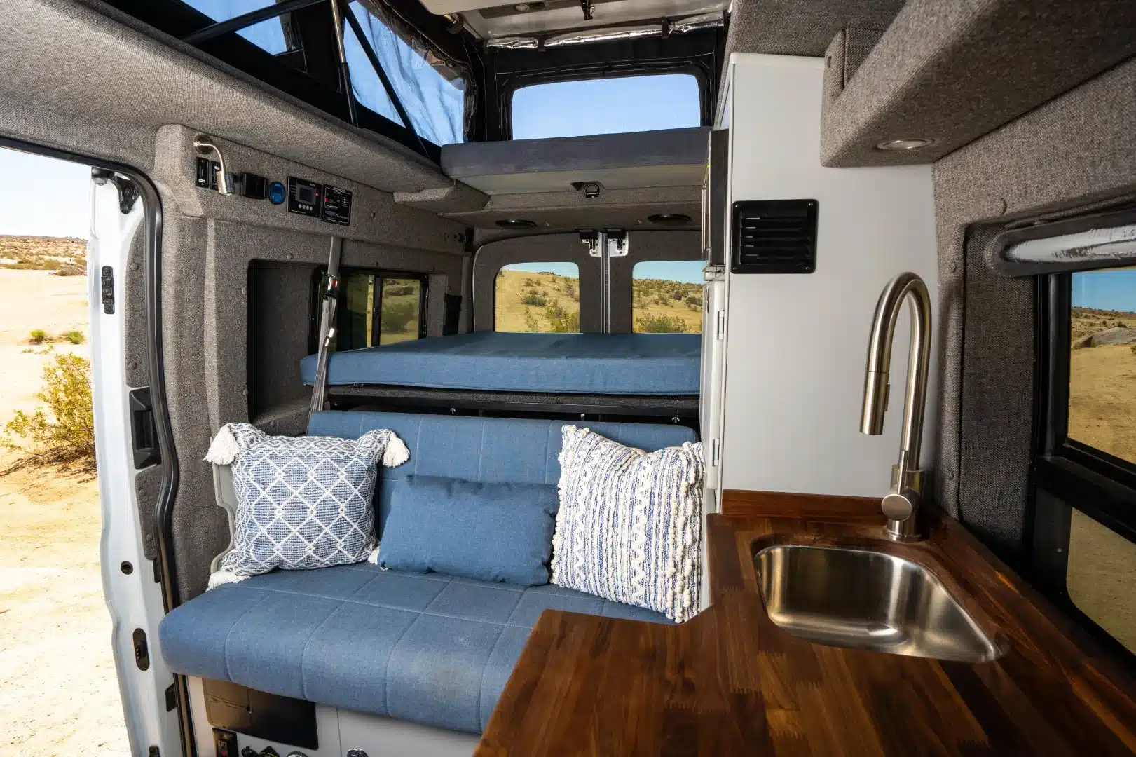 Innenraum des Tamarack Campervans mit blauem Sofa, hochklappbarem Pop-Top-Bett und Küchenzeile mit Spüle