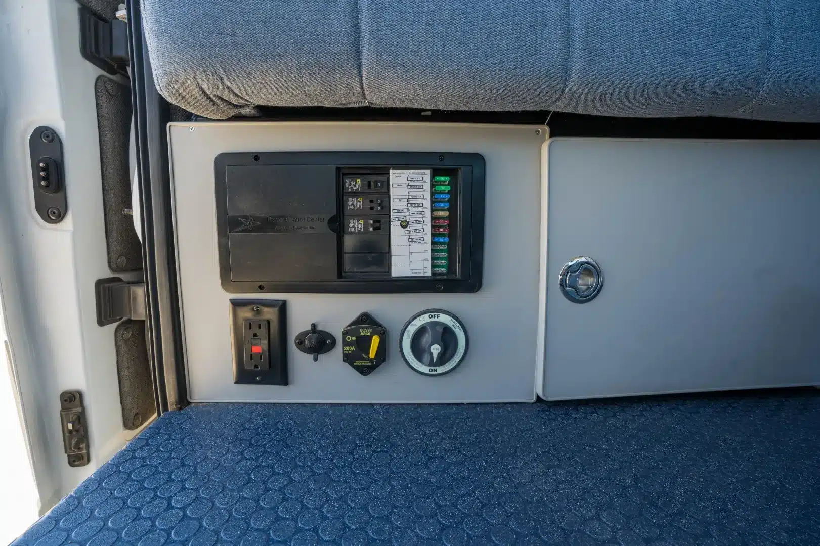 Elektrische Steuerzentrale mit Sicherungen, Steckdose und Schaltern im Innenraum des Tamarack-Campervans