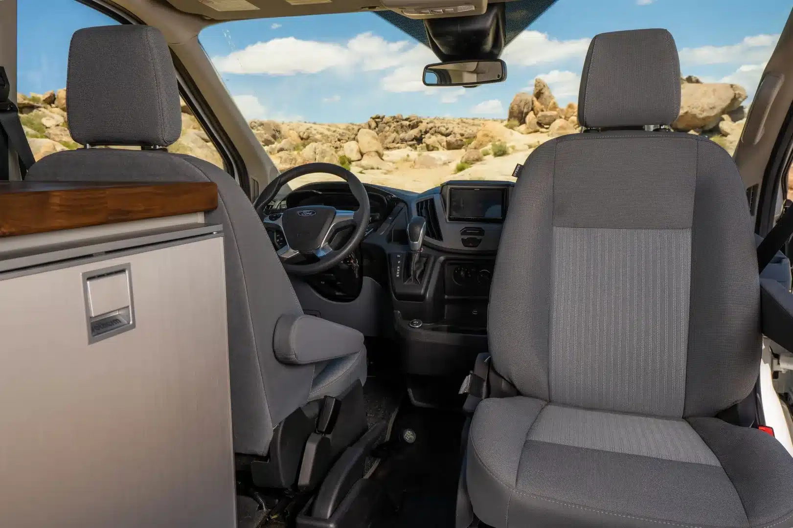 Innenraum eines Ford Transit Campervans mit Fahrerhaus, Vordersitzen und seitlichem Ausbau.