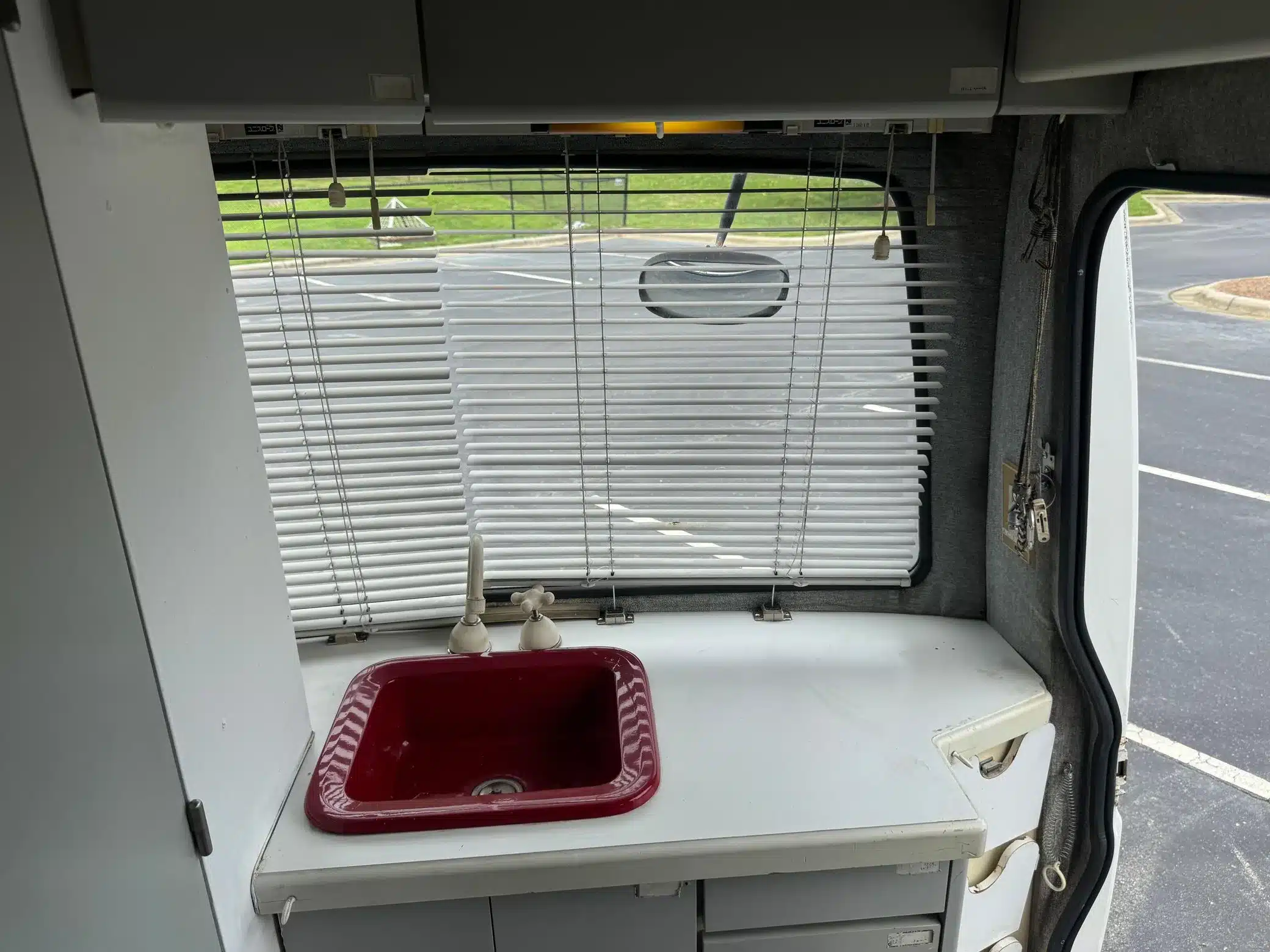 Innenraum des Toyota LiteAce Camper mit rotem Spülbecken, weißen Schränken und Jalousie