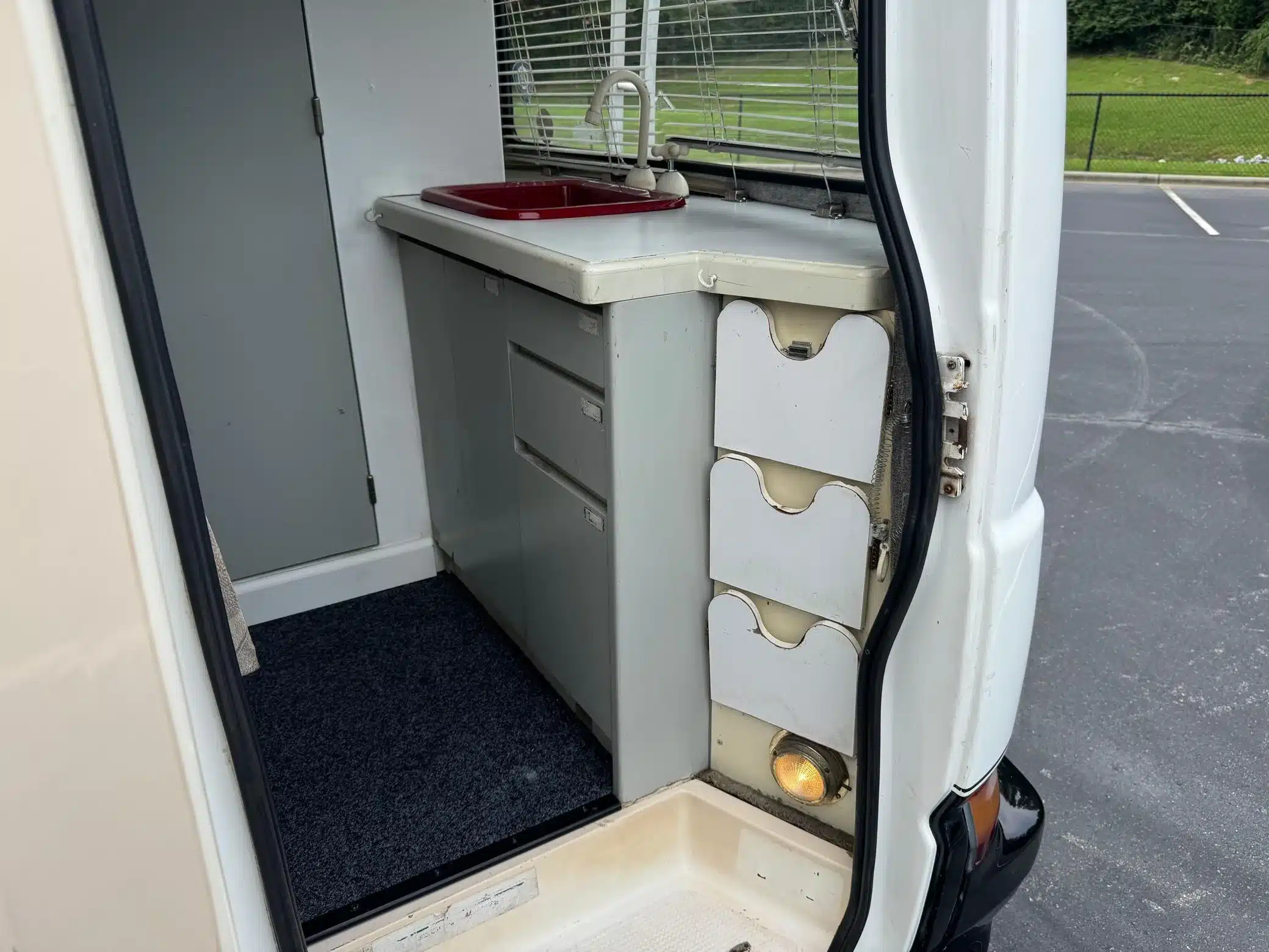 Innenraum des Toyota LiteAce Campers mit Spüle, Wasserhahn, Schubladen und grauem Teppichboden