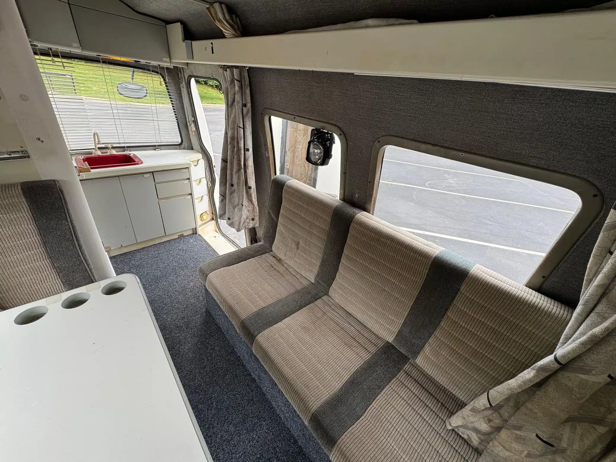 Innenraum eines Toyota LiteAce Campers mit grauen Sitzpolstern, Küchenzeile, roter Spüle und Fenstern