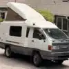 Weiß-grauer Toyota TownAce Camper von 1991 mit aufgestelltem Hubdach und 4WD-Schriftzug vor einem Wohnhaus