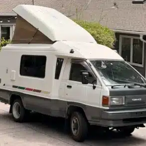 Weiß-grauer Toyota TownAce Camper von 1991 mit aufgestelltem Hubdach und 4WD-Schriftzug vor einem Wohnhaus