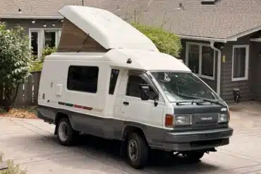 Weiß-grauer Toyota TownAce Camper von 1991 mit aufgestelltem Hubdach und 4WD-Schriftzug vor einem Wohnhaus