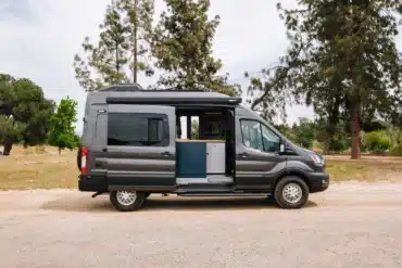 Grauer Field Van Tuolumne auf Ford-Transit-Basis mit geöffneter Seitentür in einer parkähnlichen Umgebung