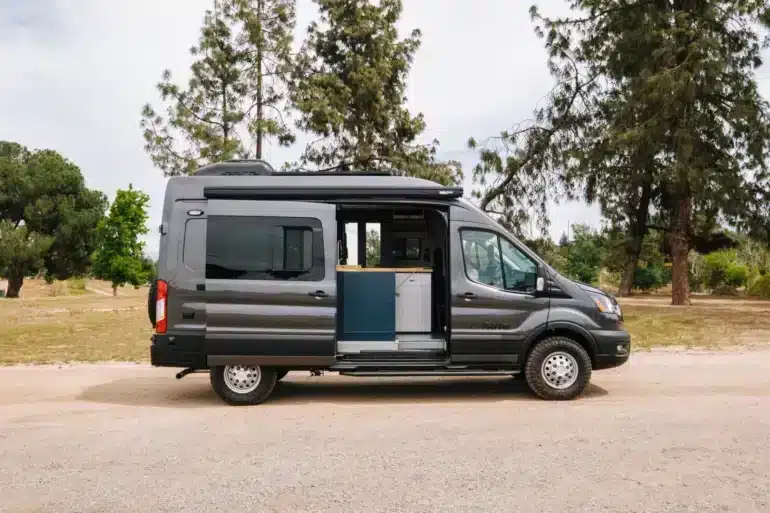 Grauer Field Van Tuolumne auf Ford-Transit-Basis mit geöffneter Seitentür in einer parkähnlichen Umgebung