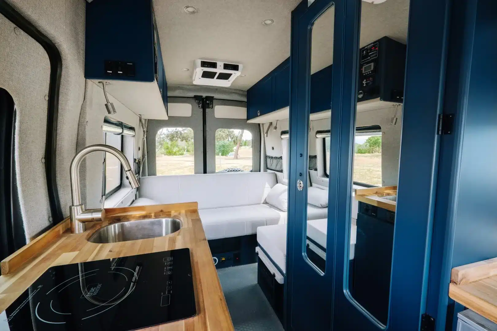 Innenraum des Field Van Tuolumne mit Induktionskochfeld, Spüle, blauem Möbelausbau und Sofa