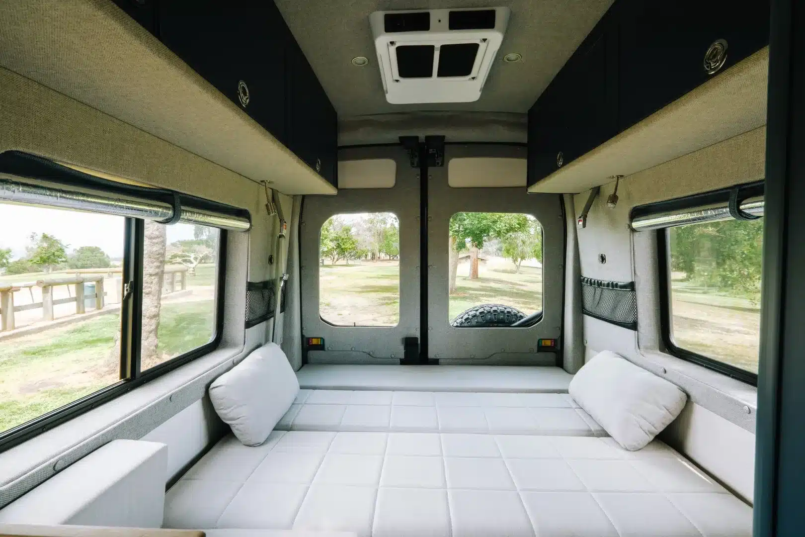 Heckbereich eines Field Van Tuolumne mit großem weißen Bett, Seitenfenstern und dunklen Oberschränken