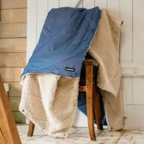 Blaue UNFOLD Kuscheldecke mit weicher Sherpa-Fleece-Seite über einem Holzstuhl