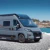 Grauer Vancona Campervan auf Fiat-Ducato-Basis vor einem Hafen mit Meer und Küstenstadt