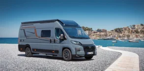 Grauer Vancona Campervan auf Fiat-Ducato-Basis vor einem Hafen mit Meer und Küstenstadt