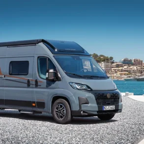 Grauer Vancona Campervan auf Fiat-Ducato-Basis vor einem Hafen mit Meer und Küstenstadt