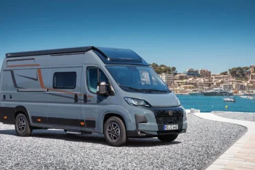 Grauer Vancona Campervan auf Fiat-Ducato-Basis vor einem Hafen mit Meer und Küstenstadt