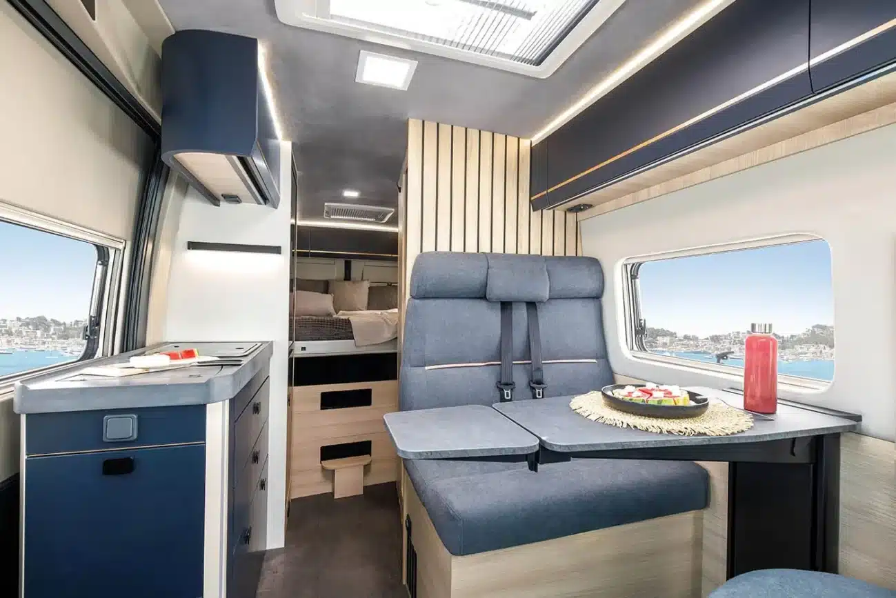 Innenraum eines Vancona Campervans mit blauen Möbeln, Sitzgruppe, Küche und Heckbett