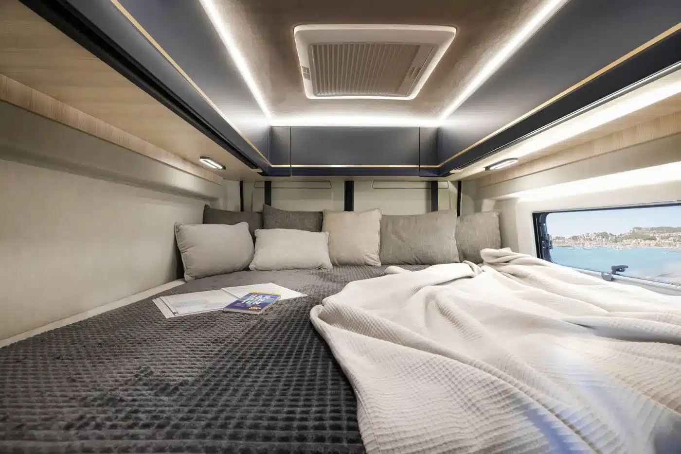 Innenansicht des Vancona Campervans mit Heckbett, Kissen, Decke und indirekter Beleuchtung