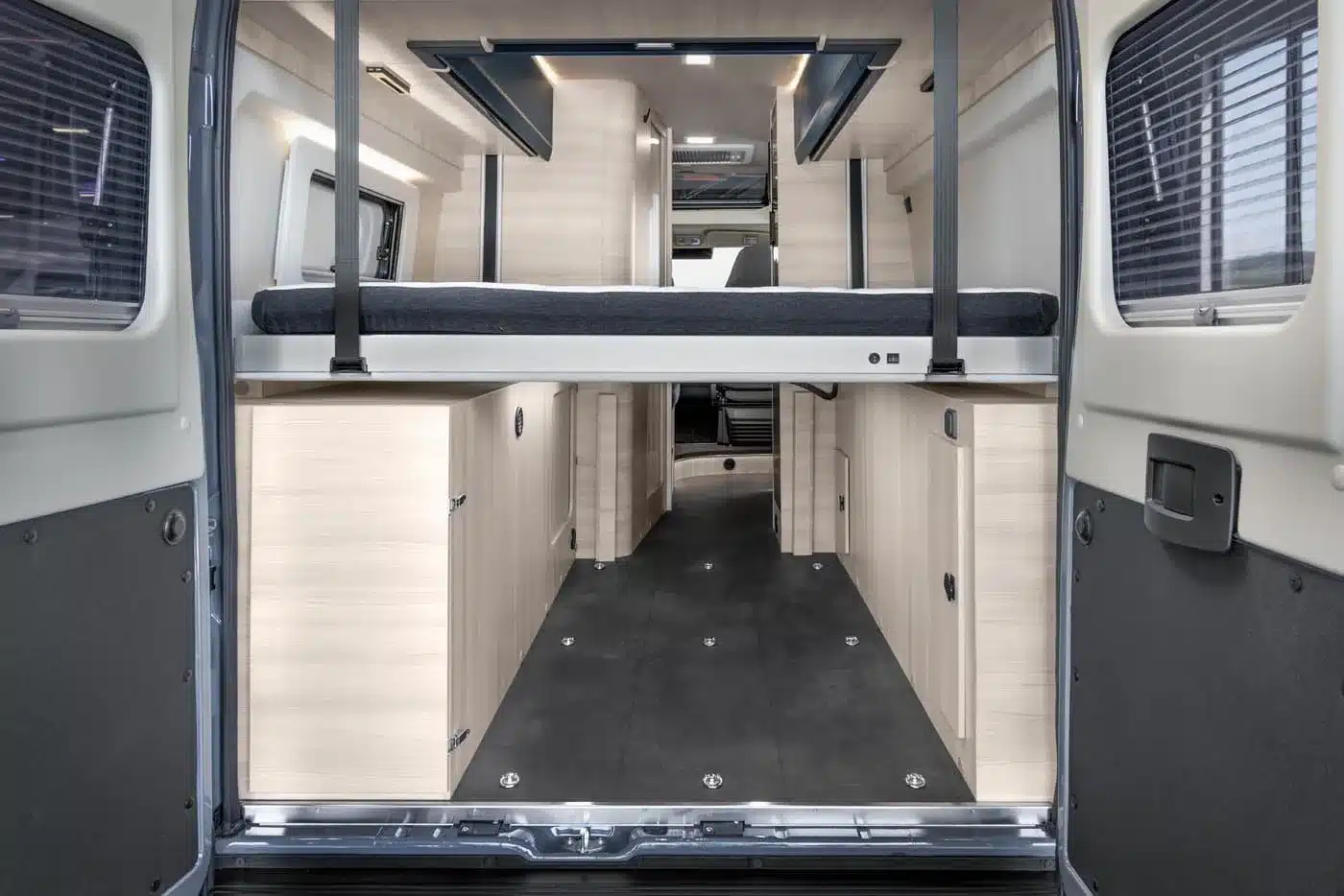 Innenraum eines Vancona Campervans mit hochgestelltem Heckbett, Holzschränken und großer Ladefläche