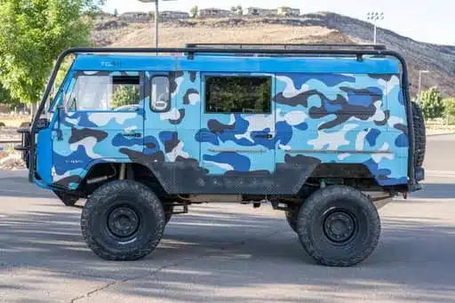 Blau camouflage-folierter Volvo C303 TGB 1111 mit grobstolligen Offroad-Reifen auf einer Straße
