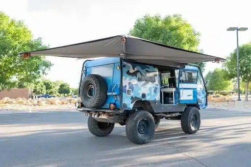 Blauer Volvo C303 TGB 1111 Camper mit Camouflage-Folierung und ausgeklappter Markise