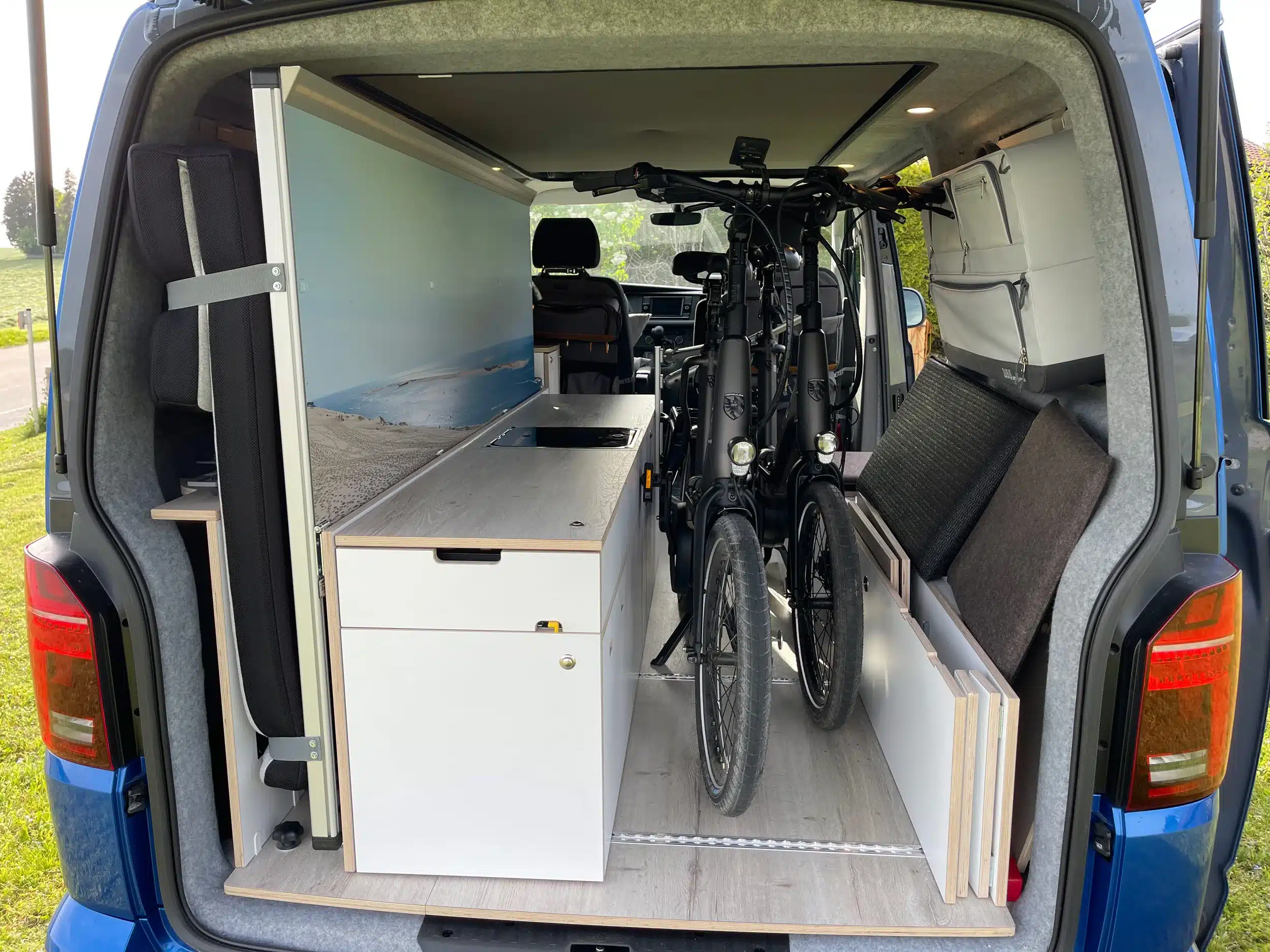 Innenraum eines blauen VW T6 mit Camperausbau, Küchenmodul, Bett und zwei Fahrrädern
