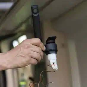 Hand hält eine schwarze Wohnmobil-Armatur mit Mikroschalter und Anschlusskabeln beim Einbau
