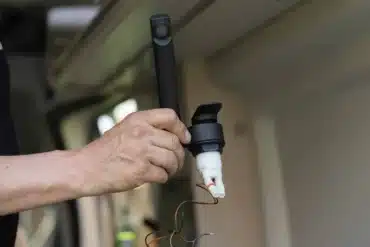 Hand hält eine schwarze Wohnmobil-Armatur mit Mikroschalter und Anschlusskabeln beim Einbau