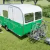 Grün-weißer Wave Wohnwagen mit Fahrradträger und zwei Fahrrädern auf einer Wiese