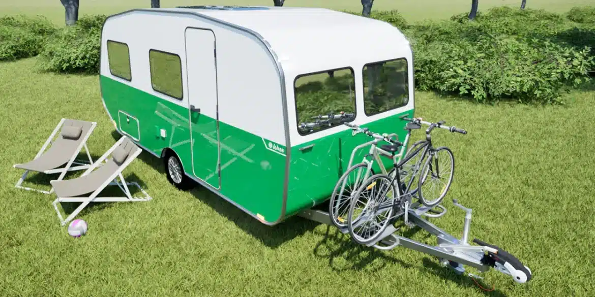 Grün-weißer Wave Wohnwagen mit Fahrradträger und zwei Fahrrädern auf einer Wiese