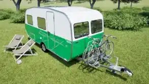 Grün-weißer Wave Wohnwagen mit Fahrradträger und zwei Fahrrädern auf einer Wiese