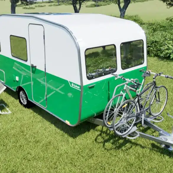 Grün-weißer Wave Wohnwagen mit Fahrradträger und zwei Fahrrädern auf einer Wiese