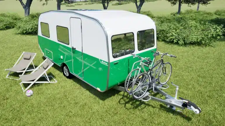 Grün-weißer Wave Wohnwagen mit Fahrradträger und zwei Fahrrädern auf einer Wiese