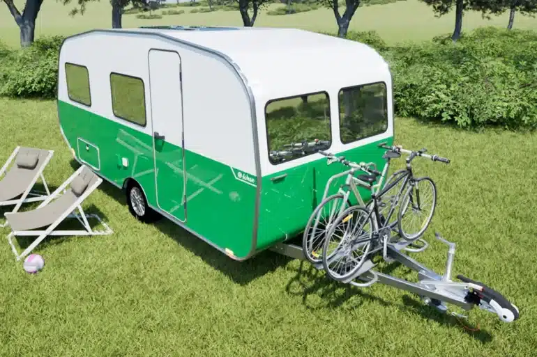 Grün-weißer Wave Wohnwagen mit Fahrradträger und zwei Fahrrädern auf einer Wiese