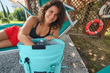 Türkiser YETI Hopper M20 Kühlrucksack mit geöffneter Kühlöffnung neben einer Frau im Garten
