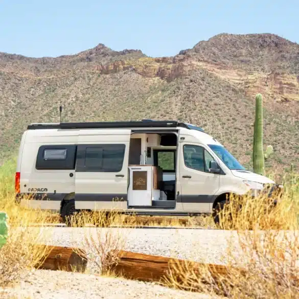 Weißer Papago Vans Zion Campervan mit geöffneter Schiebetür in einer trockenen Wüstenlandschaft