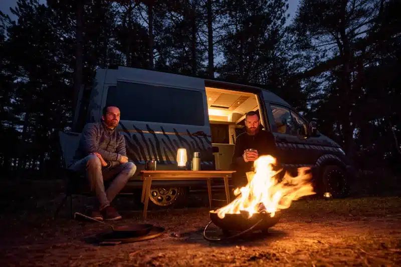 Custom-Bus Camper XL mit geöffneter Schiebetür und Lagerfeuer im Wald
