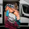 Frau hält eine farbenfrohe All-Terrain-Bettdecke an der geöffneten Schiebetür eines weißen Vans.